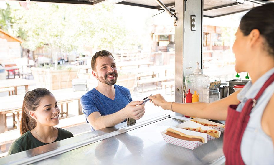 A woman at a food stand handing a customer back his credit card 