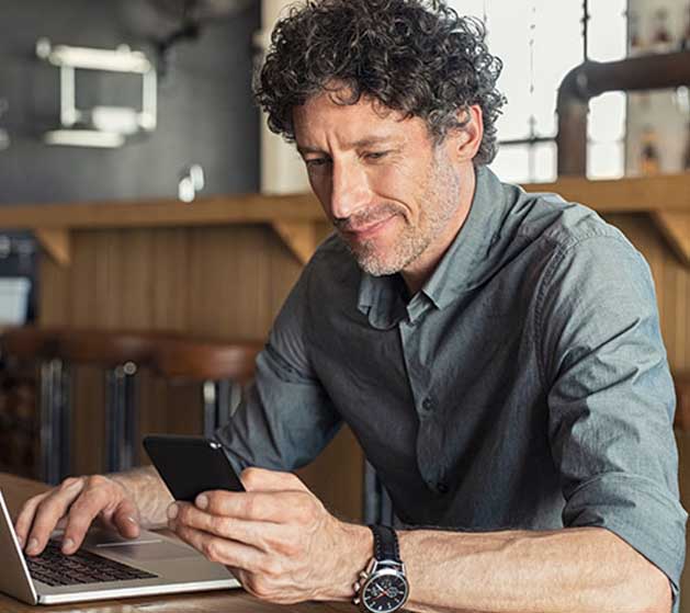 A man reviewing business performance on his laptop and iPhone using North's merchant portal services