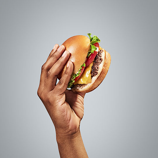 A hand holding a cheese burger representing the quick-service hospitality industry