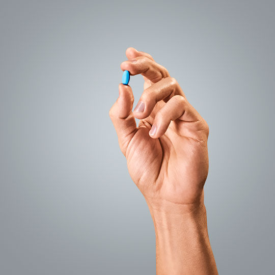 A hand holding a small blue pill representing the healthcare industry