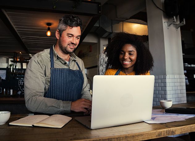 A man and a woman at a coffeeshop counter looking at a laptop